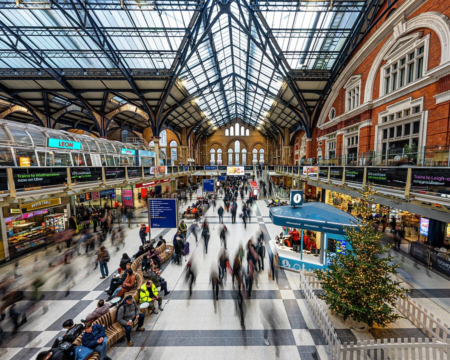 Travelers move through a busy train station beneath a grand arched glass ceiling.